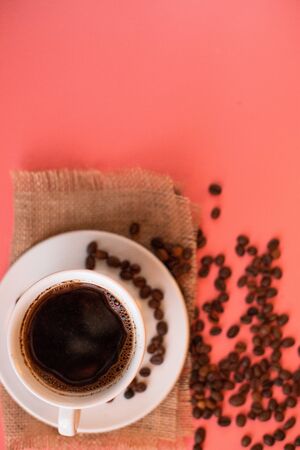 A white Cup of coffee with a saucer on a pink background scattered coffee beans.の写真素材