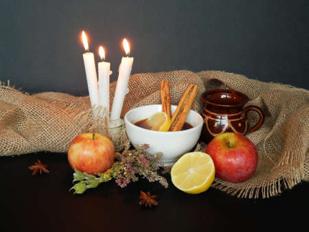 Autumn background with apples, pear, dry herbs, anise, cinnamon sticks, a cup of tea, candles,...