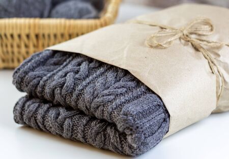 Handmade gray sweater is packed in kraft paper. Handmade knitted sweater. In the background is a wicker basket with knitting needles.の写真素材