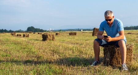 Adult man with a phone sits on a haystack.の写真素材