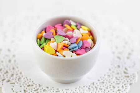 Candies in the form of multi-colored hearts lie in a white plate. Place for text.の写真素材