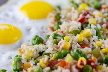 Rice with vegetables pepper, peas, corn and fried eggs on a plate. Place for text.の写真素材
