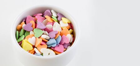 Candies in the form of multi-colored hearts lie in a white plate. Place for text.の写真素材