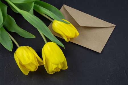 Yellow tulip near a blank greeting card and envelopes on a black background with space for text.の写真素材
