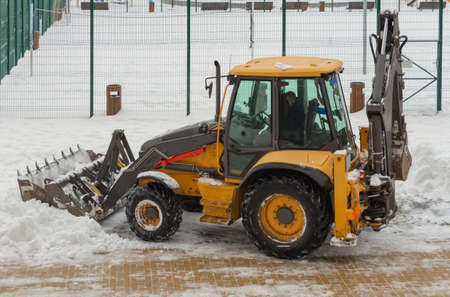 A small tractor clears snow from the road near the house.