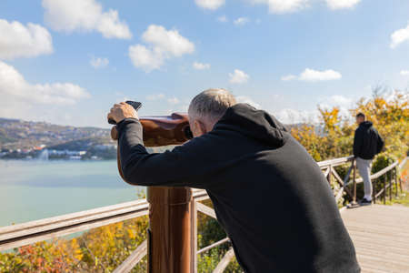 A man looks through a tourist telescope at the lake and mountains. Autumn landscape.の写真素材