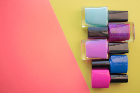Bottles of nail polish. A group of bright manicures on a pink, yellow background. With empty space on the left. View from aboveの写真素材
