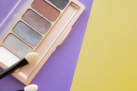 Cosmetic accessories. A brush, eyeshadow on a yellow, purple background. With empty space on the right. View from aboveの写真素材