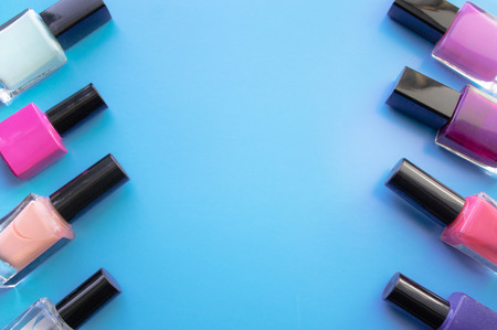 Bottles of nail polish. A group of bright nail polishes on a blue background. With empty space in the middle. View from aboveの写真素材