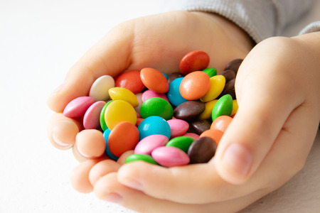 Round, multi-colored, chocolates. Close-up. A pile of multi-colored candies. A child holds a candy.の写真素材