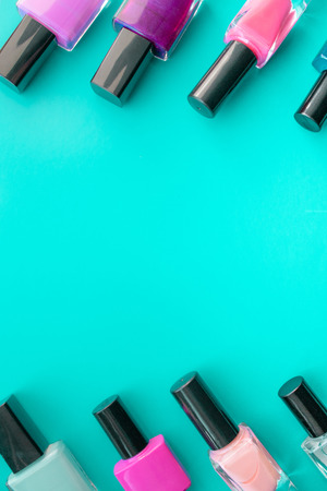 Bottles of nail polish. A group of bright nail polishes on a green background. With empty space in the middle. View from aboveの写真素材