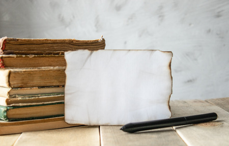 Old books on the table. A white sheet of paper burned around the edges. Place for your text. Concept background.の写真素材