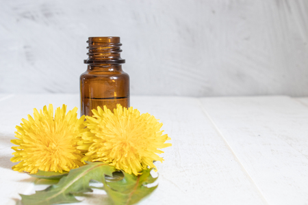 Natural essential oil in a glass bottle with fresh dandelion flowers on the table. Flower essential oil. Phytotherapy.の写真素材