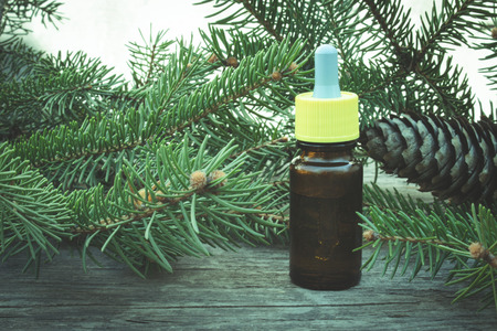 Essential oil of pine in a glass bottle with coniferous pine leaves on a wooden table.の写真素材