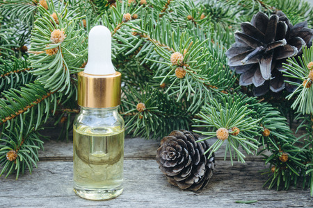 Essential oil of pine in a glass bottle with coniferous pine leaves on a wooden table.の写真素材