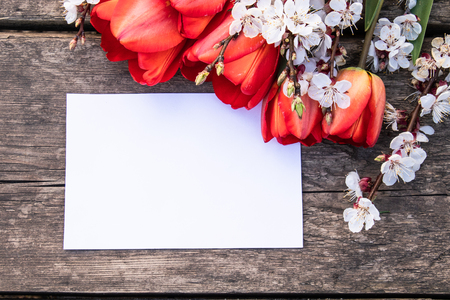 A bouquet of red tulips and branches of white flowers on old wooden boards. Place for text. The concept of spring has come. View from above. Banner March 8, Easterの写真素材