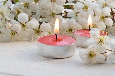 A candle stands on a wooden white table near the branches of white flowers of cherry. close-up.の写真素材