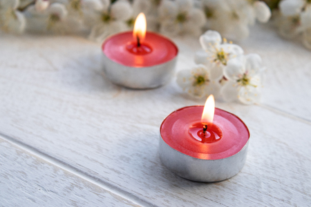 A candle stands on a wooden white table near the branches of white flowers of cherry. close-up.の写真素材