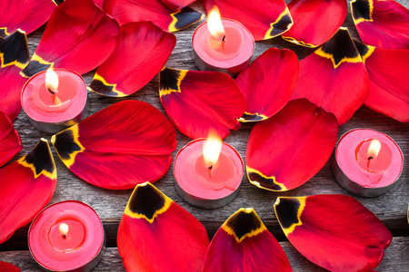 Red, burning candles near the red tulip petals. Fallen tulip petals on the table.の写真素材