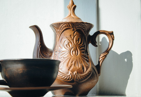 A teapot and a cup of clay are standing near the window. Close-up.の写真素材