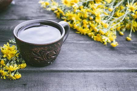 A cup of tea from yellow daisies with a bouquet of daisies on a wooden background. Close-up.の写真素材