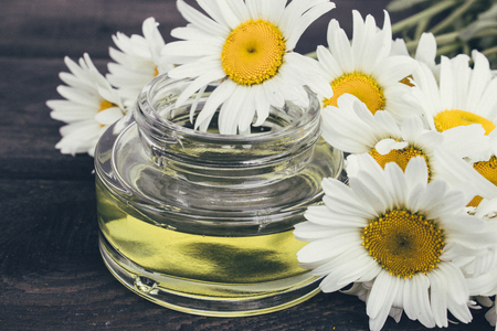 A can of light essential oil from chamomiles stands on dark boards near chamomile flowers.の写真素材
