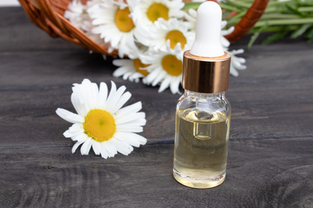 Chamomile essential oil in a glass bottle with a pipette stands on wooden boards near a basket with daisy flowers.の写真素材
