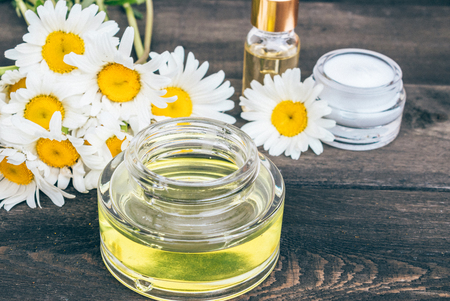 Essential oil and cosmetic cream are on the wooden table near the chamomile flowers.の写真素材