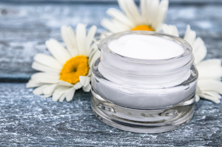 Cosmetic cream in a glass jar stands near chamomile flowers.の写真素材
