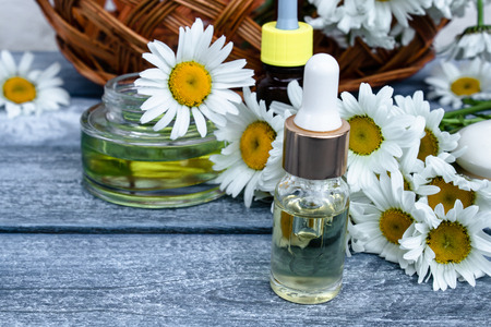 Chamomile essential oil in a glass jar and bottles near the daisies on a blue background.の写真素材