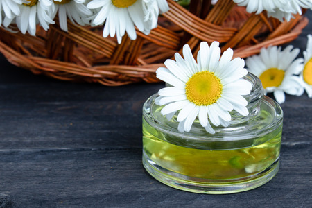 On dark boards near the basket with chamomile flowers there is a bank of light chamomile essential oil.の写真素材
