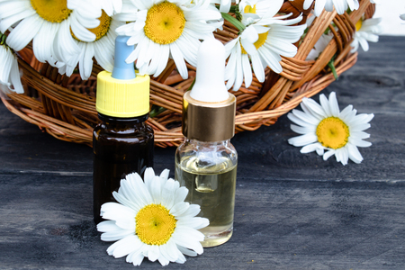 Chamomile essential oil in a glass bottle with a pipette stands on wooden boards near a basket with daisy flowers.の写真素材