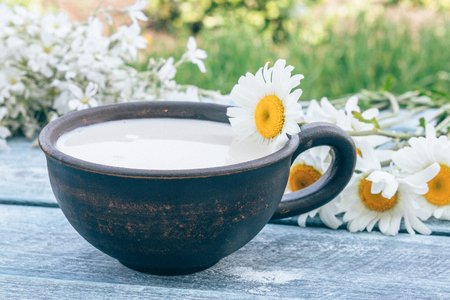 Next to the white daisies there is a cup with milk on a blue background. Close-up.の写真素材