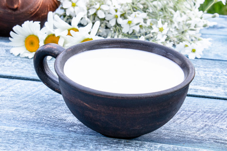 Next to the white daisies there is a cup with milk on a blue background. Close-up.の写真素材
