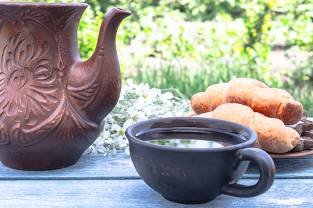 Next to the croissants and white flowers near the jug is a cup of tea.の写真素材