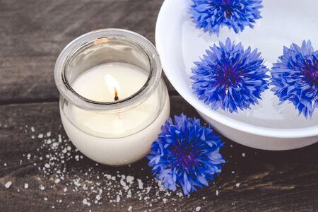 blue cornflowers lie in the water in a white bowl near a burning candle on the background of old boards. close-upの写真素材