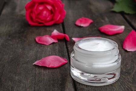 Natural flower cosmetics with red pink flowers for face and body care in a glass jar on a wooden rustic background, toned imageの写真素材