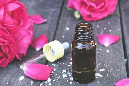 Essential oil with red rose petals on a dark wooden background. Aromatherapy.の写真素材