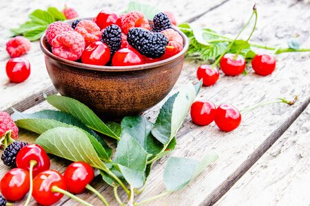 juicy fresh delicious berries raspberries, cherries, mulberries in a bowl on wooden background. Close-upの写真素材