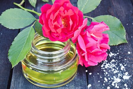 Glass jar with essential oil and red roses on a dark wooden background. Aromatherapy.の写真素材
