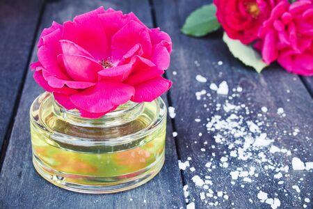 Bottle of fragrant oil with red roses on a wooden table. Aromatherapy.の写真素材