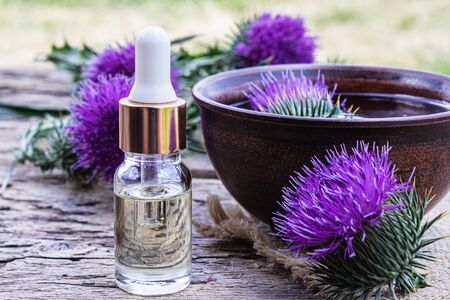 A bottle of tincture or potion's essential oil and flowers of thistle on a wooden background.の写真素材