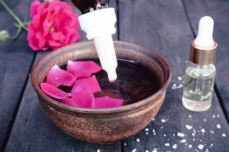 Bowl with red rose petals on a background of dark wooden boards and essential oil with roses. Aromatherapy.の写真素材