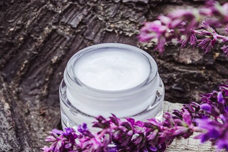 Cosmetic cream in a glass jar on a wooden background with lavender wildflowers. Face cream. Body care.の写真素材