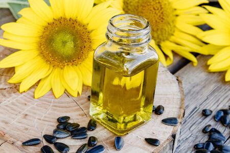 Organic sunflower oil in a glass jar with seeds and fresh flowers on a wooden background. Healthy foods and fats. Organic and eco food.の写真素材