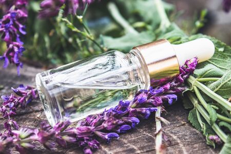 Lavender essential oil in a glass bottle on a wooden table near the branches of blooming lavender. Tincture or essential oil with lavender. Spa herbal medicine.の写真素材