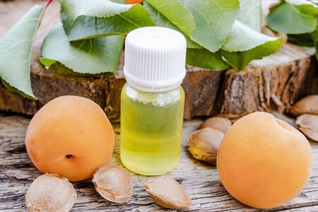 Apricot oil in a small jar near ripe yellow apricot on a wooden table. Selective focus.の写真素材