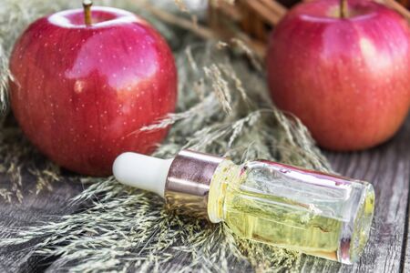 Apple essential oil on a wooden table near ripe red apples. Essential oil is used to fill lamps, perfumes and in cosmetics. Close-up.の写真素材