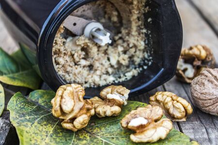 chopped walnut in a coffee grinder near the walnut kernel on an old wooden table. Eco food.の写真素材