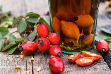 Glass bottle with tincture or a drink with rose hips on a wooden table near the red berries of rose hips. Phytotherapy.の写真素材
